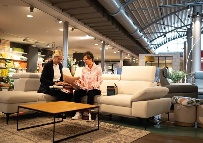Zwei Personen sitzen auf hellem Sofa mit Couchtisch in einer Möbelhaus Ausstellung